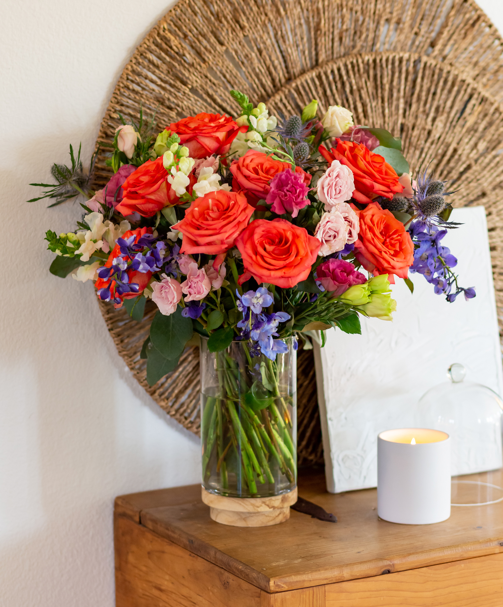 Vibrant floral arrangement featuring coral roses, purple blooms, and greenery in a glass vase.