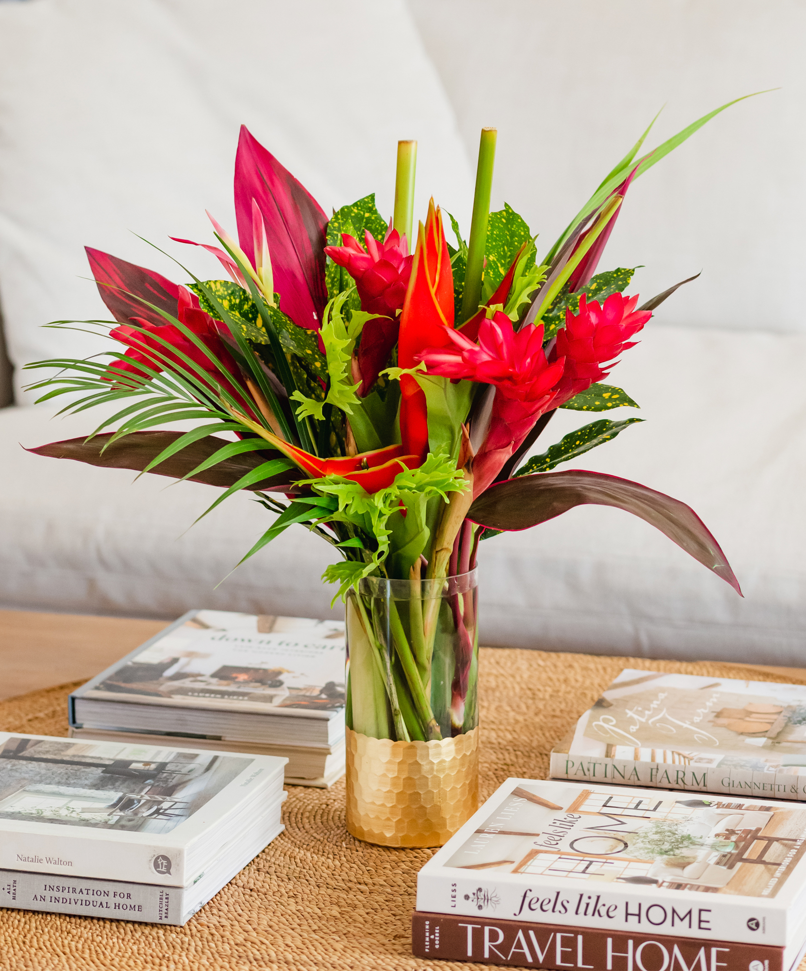 Vibrant tropical flower arrangement featuring red blooms and lush green foliage in a stylish vase.