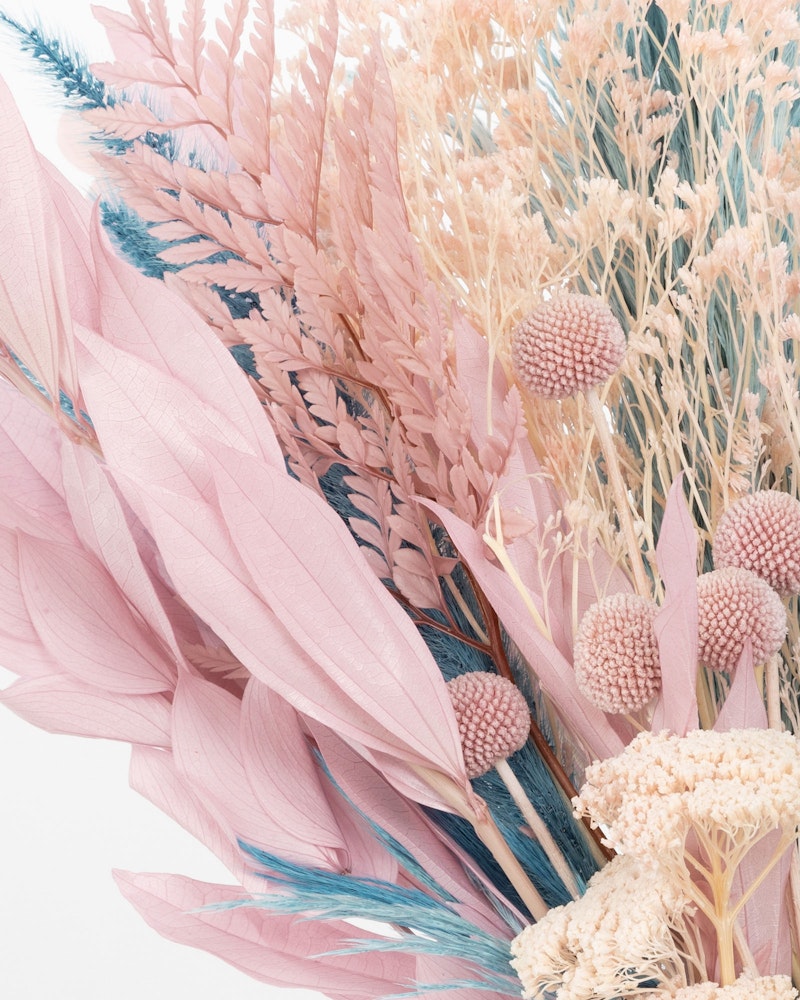 A close-up of a delicate bouquet featuring an array of dyed pink and cream dried flowers, including feathery plumes and textural seed heads.