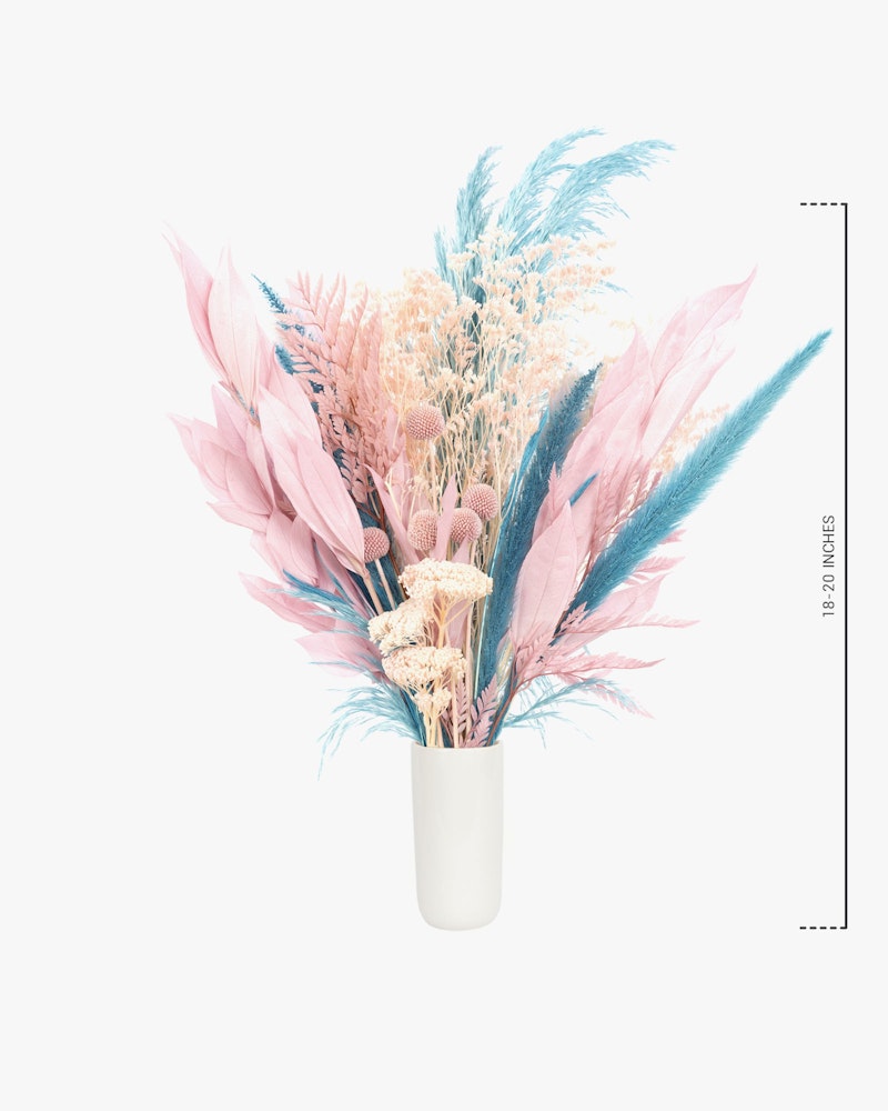 A vibrant bouquet of pink and blue dried flowers and pampas grass arranged in a modern white vase against a clean white background, with a ruler for scale.