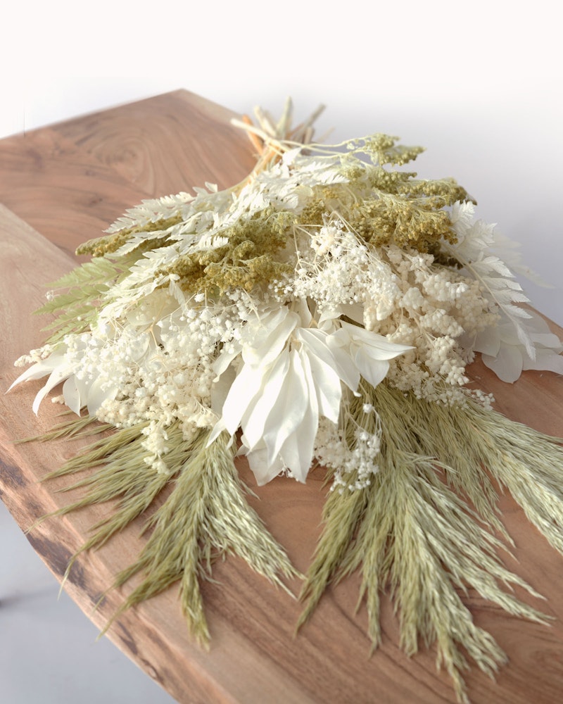 Elegant floral arrangement with white flowers and dried grass on a wooden cutting board against a white background, showcasing a rustic home decor style.
