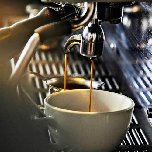 Close-up of an espresso machine brewing a fresh cup of coffee, with steam rising above the white cup as golden brown coffee flows from the portafilter.