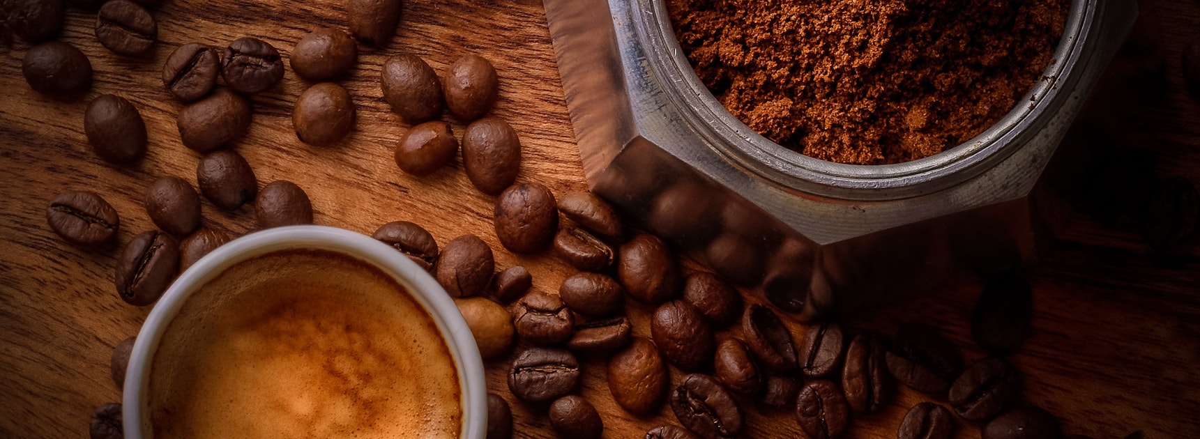 Rich espresso in a white cup, surrounded by coffee beans and ground coffee.