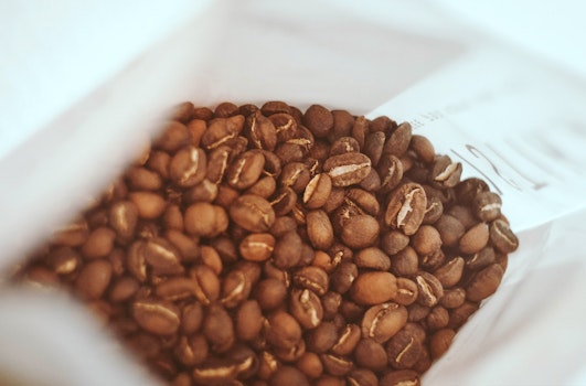Close-up view of a freshly opened bag of whole coffee beans, showcasing the texture and rich brown color of the beans, suggesting a fresh aroma and taste.
