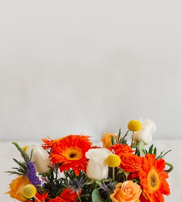 Vibrant floral arrangement featuring orange gerbera daisies, roses, and cheerful yellow accents.