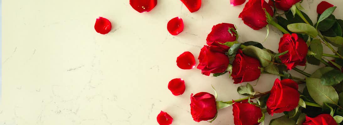 Vibrant red roses scattered with rose petals on a smooth marble surface, ideal for romance.