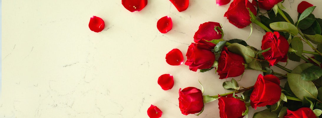 Vibrant red roses scattered with rose petals on a smooth marble surface, ideal for romance.