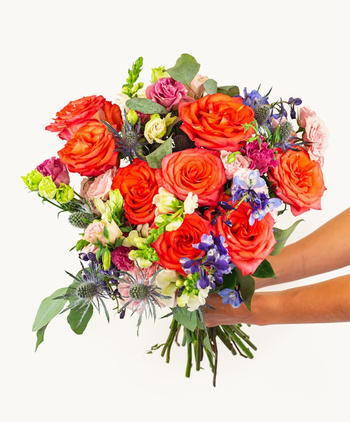 Vibrant bouquet featuring orange roses, purple flowers, and lush greenery, beautifully crafted.