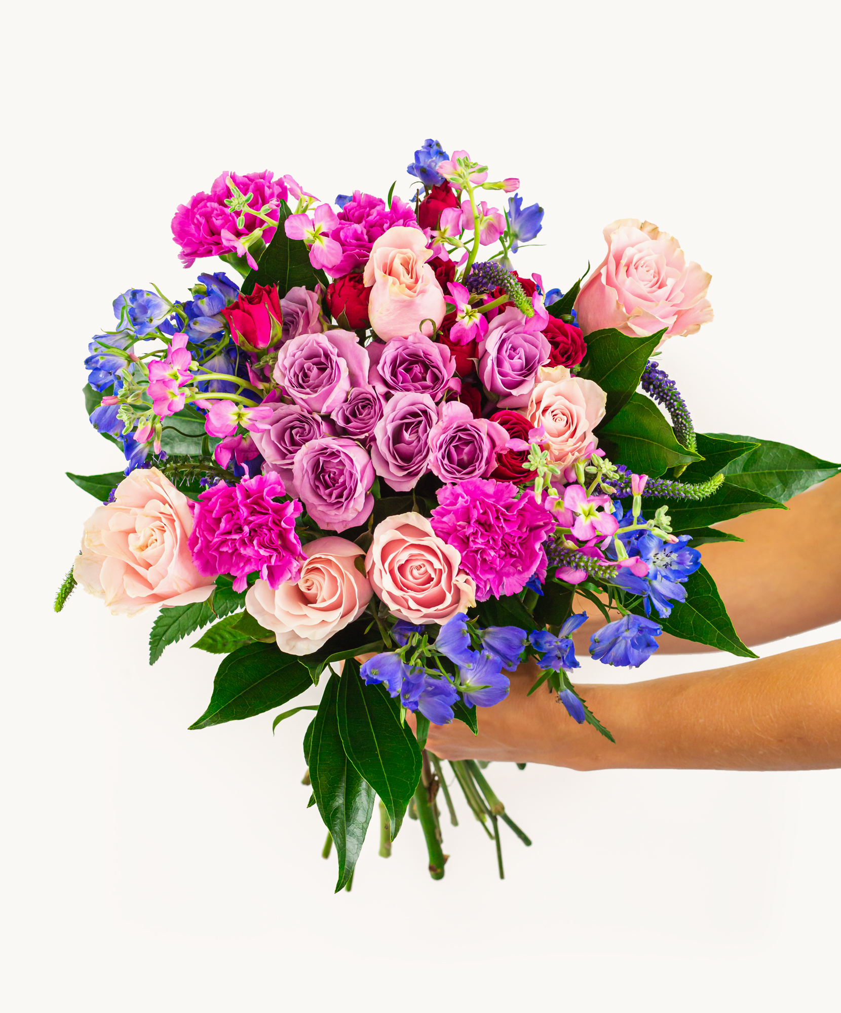 Vibrant hand-held bouquet featuring pink and purple roses, carnations, and blue flowers.
