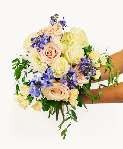 A vibrant bouquet featuring soft peach roses, purple blooms, and lush greenery, elegantly arranged.