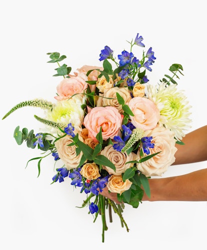 A vibrant flower bouquet featuring peach roses and blue delphiniums, perfect for celebrations.