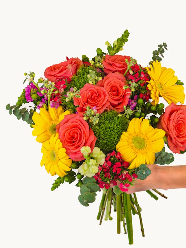 Vibrant bouquet of flowers featuring orange roses, yellow daisies, and various greenery held by a person against a white background, symbolizing freshness and natural beauty.