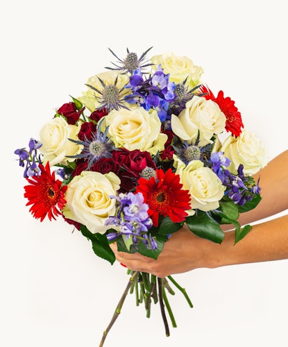 Hand-held bouquet featuring white roses, red gerberas, and blue flowers, perfect for any occasion.