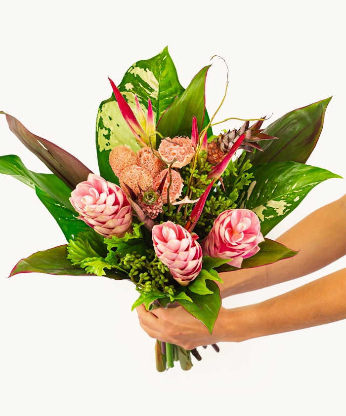 Vibrant floral bouquet featuring pink ginger flowers and tropical foliage, elegantly held.
