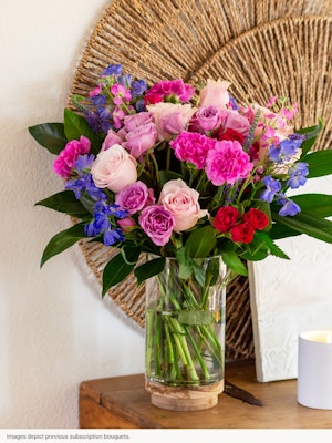 Vibrant mixed bouquet featuring pink roses, lavender blooms, and lush greens in a glass vase.