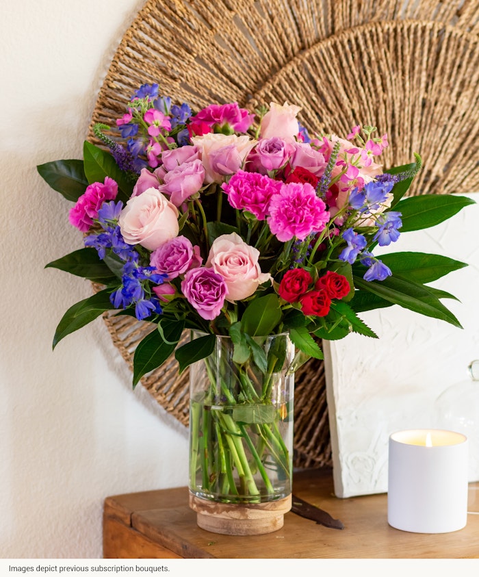 Vibrant mixed bouquet featuring pink roses, lavender blooms, and lush greens in a glass vase.