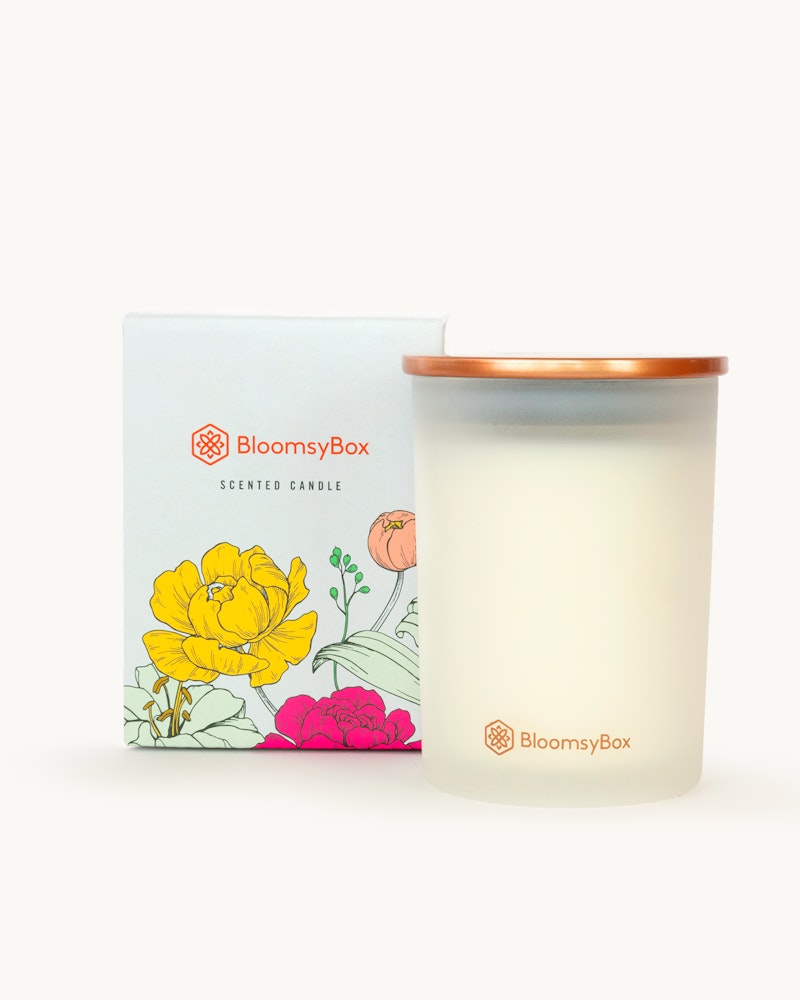 A BloomsyBox scented candle with a wooden lid, displayed next to its floral-patterned box on a white background, reflecting a serene, minimalist aesthetic.