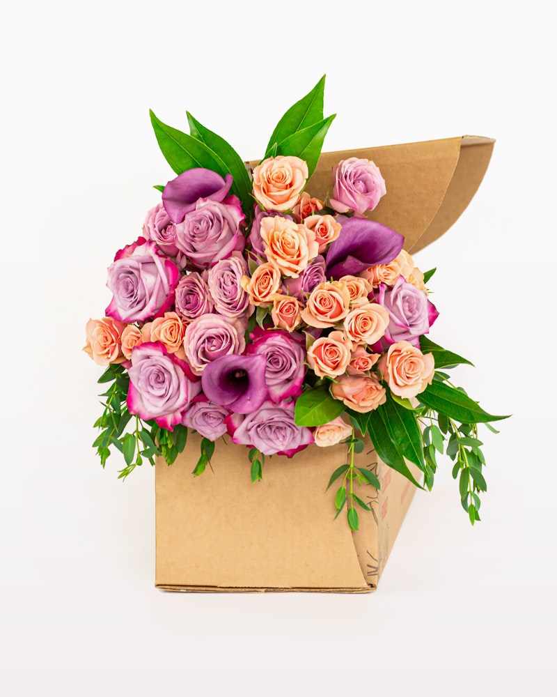 Bouquet of flowers with pink roses and purple calla lilies presented in a stylish brown paper cone against a white background, perfect for a gift or decoration.