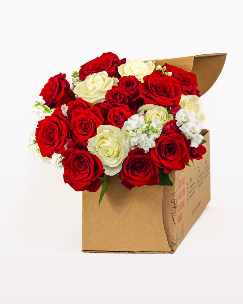 A bouquet of vibrant red roses and delicate white flowers packaged neatly in a brown cardboard box against a white background, symbolizing a romantic gift or gesture.