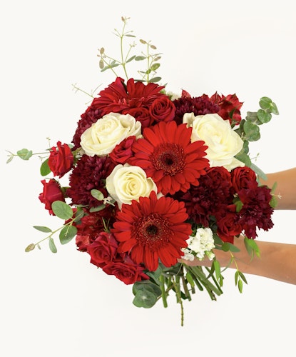 Vibrant bouquet featuring red gerbera daisies, roses, and rich greenery in a beautiful arrangement.