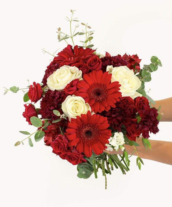 Vibrant bouquet featuring red gerbera daisies, roses, and rich greenery in a beautiful arrangement.