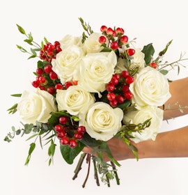 Elegant white rose bouquet adorned with vibrant red berries and lush greenery.
