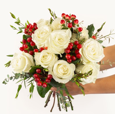 Elegant white rose bouquet adorned with vibrant red berries and lush greenery.