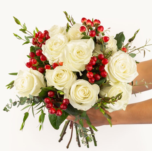 Elegant white rose bouquet adorned with vibrant red berries and lush greenery.