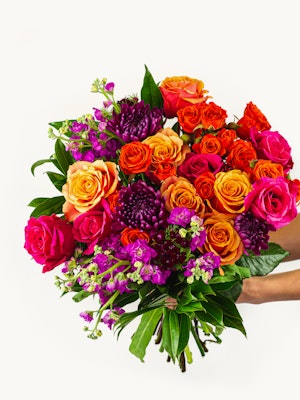 Vibrant bouquet featuring orange, pink, and purple roses with lush greenery, ideal for celebrations.