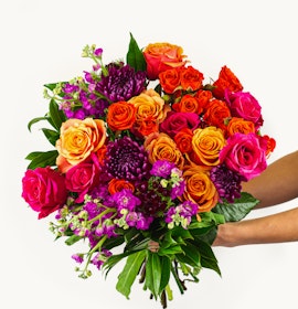 Vibrant bouquet featuring orange, pink, and purple roses with lush greenery, ideal for celebrations.