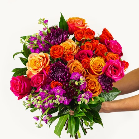 Vibrant bouquet featuring orange, pink, and purple roses with lush greenery, ideal for celebrations.