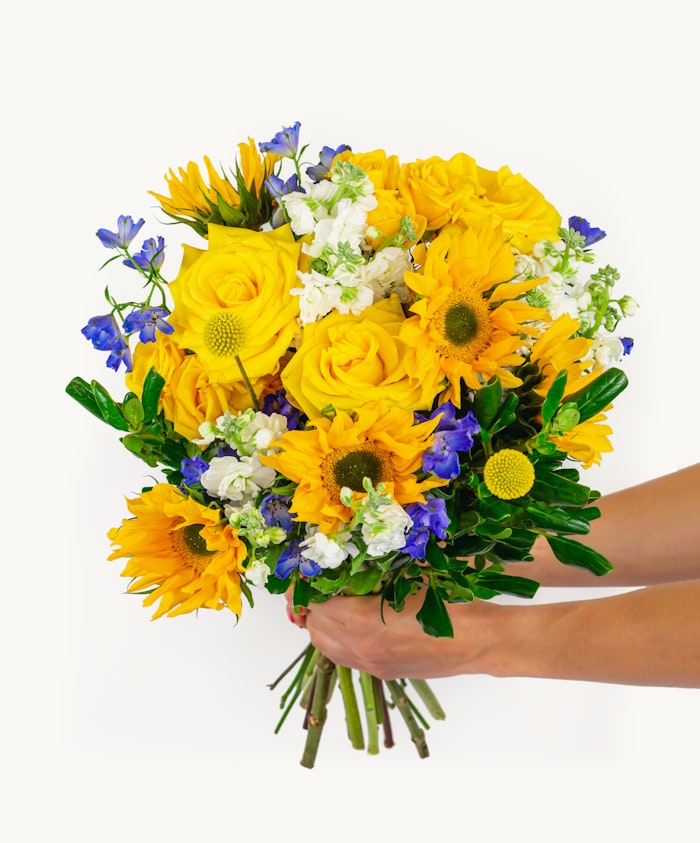 Bright floral bouquet featuring sunny yellow roses, sunflowers, and vibrant blue blooms.
