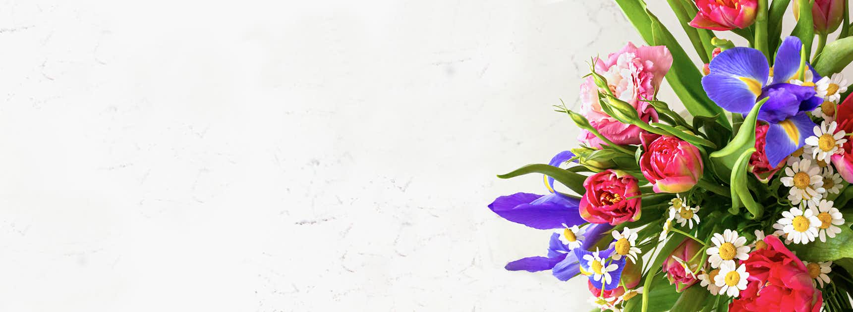 Vibrant floral arrangement featuring pink roses, daisies, and purple irises on a light background.