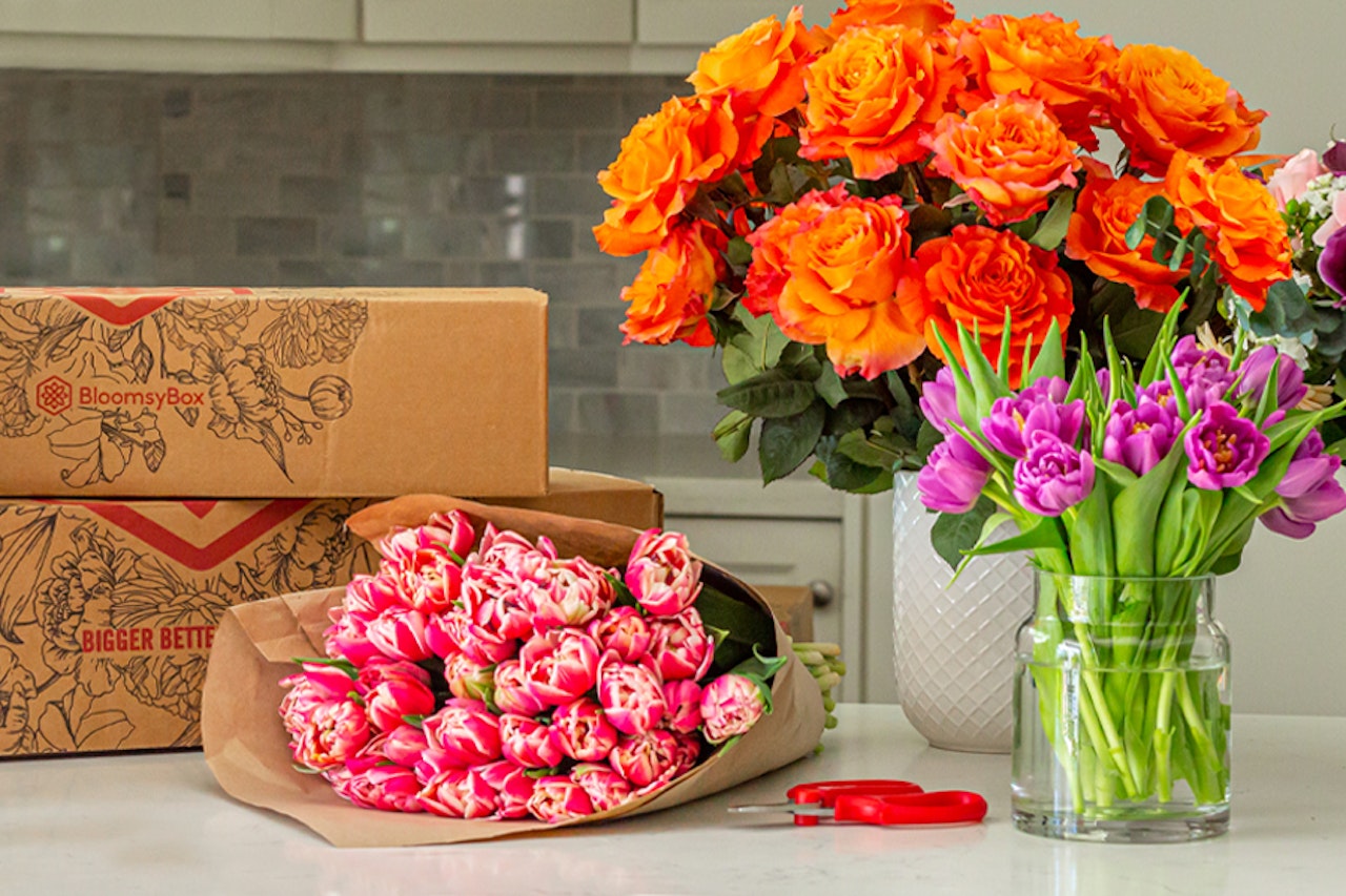 Vibrant orange roses, pink tulips, and fresh greenery in elegant arrangements on a table.