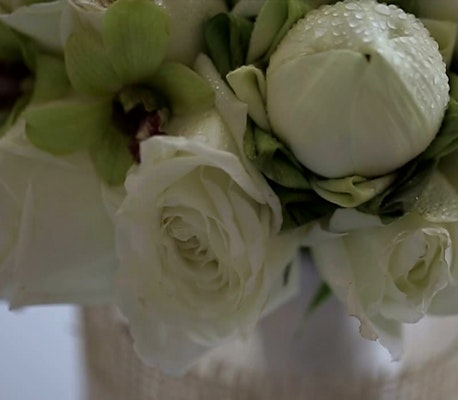 Close-up of a bouquet with creamy white roses and green orchids, with water droplets on petals, showcasing delicate floral details and soft textures.