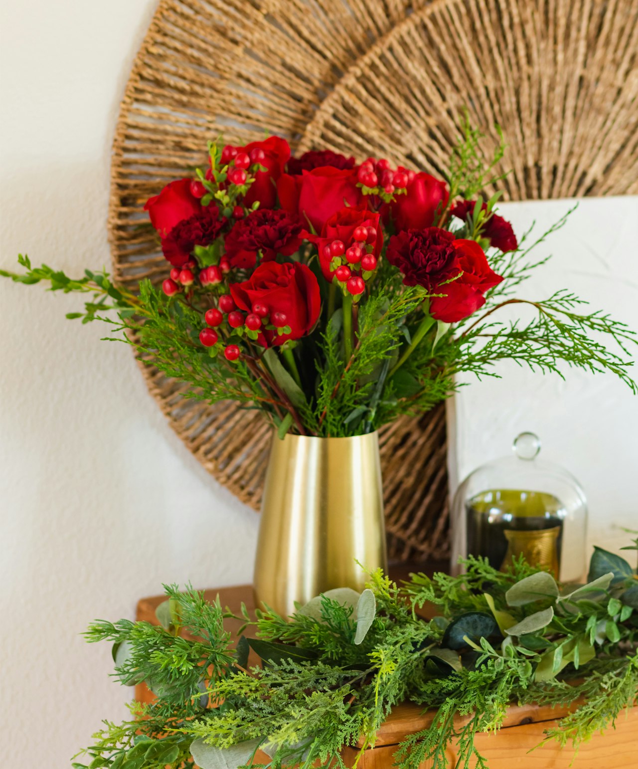 A vibrant arrangement of red roses and greens in a chic gold vase, perfect for any decor.