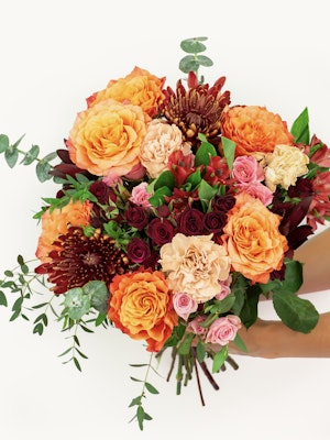 Vibrant autumn bouquet featuring orange roses, burgundy chrysanthemums, and lush greenery.