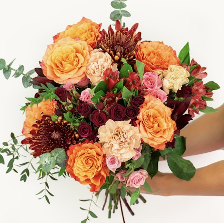 Vibrant autumn bouquet featuring orange roses, burgundy chrysanthemums, and lush greenery.