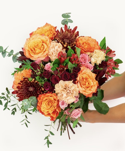 Vibrant autumn bouquet featuring orange roses, burgundy chrysanthemums, and lush greenery.