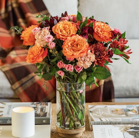 Vibrant floral arrangement featuring orange roses and assorted blooms in a glass vase.