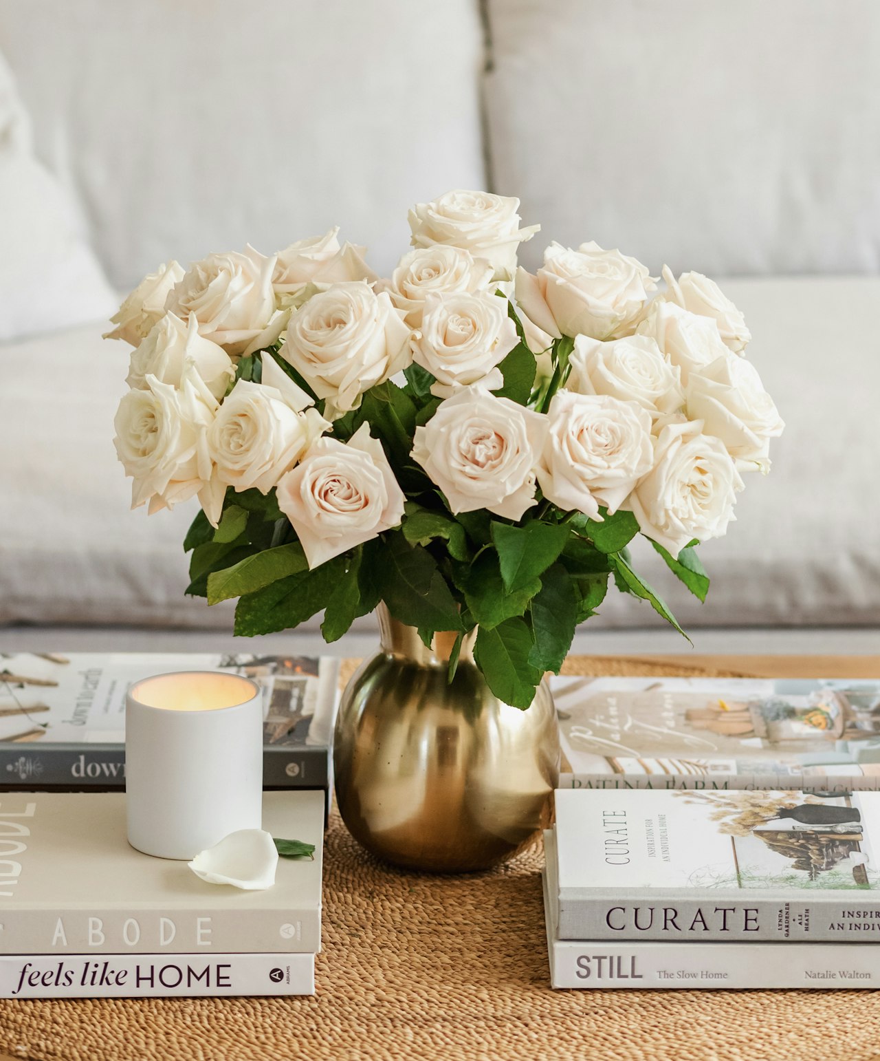 Elegant white rose bouquet in a gold vase, surrounded by stylish decor and books on a cozy table.