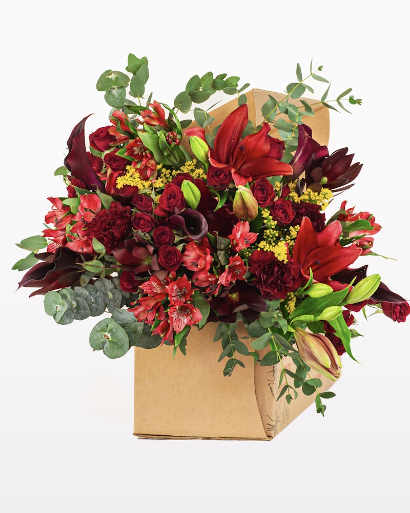 Vibrant bouquet of red flowers with green foliage in a brown paper bag, including roses and lilies against a white background, perfect for a romantic gift or decoration.