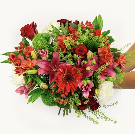 Vibrant mixed floral bouquet featuring red roses, pink lilies, and lush greenery.