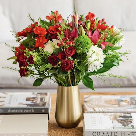 Vibrant floral arrangement featuring red roses, lilies, and greenery in a chic vase.
