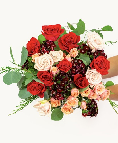 Vibrant floral bouquet featuring red, pink, and cream roses surrounded by lush greenery.