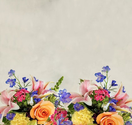 Vibrant bouquet of flowers at the bottom with pink lilies, yellow roses, and blue delphiniums against a soft beige background with ample copy space.