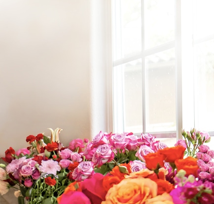 Vibrant floral arrangement featuring assorted roses and colorful blooms by a sunny window.