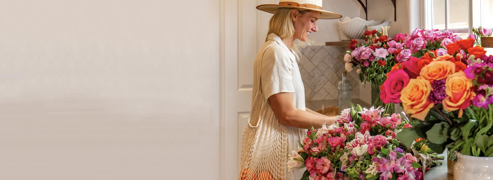 A woman in a stylish hat arranging vibrant flowers in a bright, cheerful space.