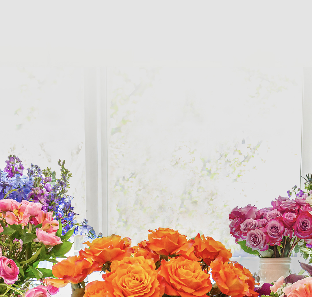 Vibrant floral arrangements with orange roses, pink blooms, and lush greenery by a sunny window.