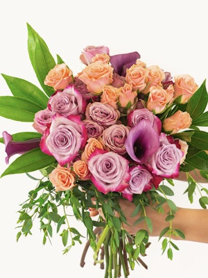 Vibrant bouquet featuring pink and purple roses with lush green leaves, elegantly held.